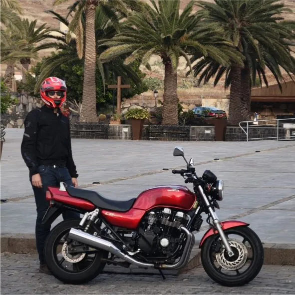 Client with a motorcycle stopped in Vega de Río Palmas in Fuerteventura, with Canary Island palm trees and an authentic island landscape in the background during a motorcycle tour.
