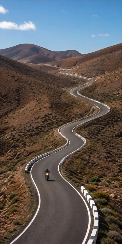 Motorcycle riding along a winding mountain road in Fuerteventura with scenic volcanic landscape views during a tour.