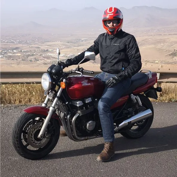 Rider on a red retro Honda CB750 parked on the road ascending to Betancuria, with panoramic views of northern Fuerteventura during a motorcycle tour.