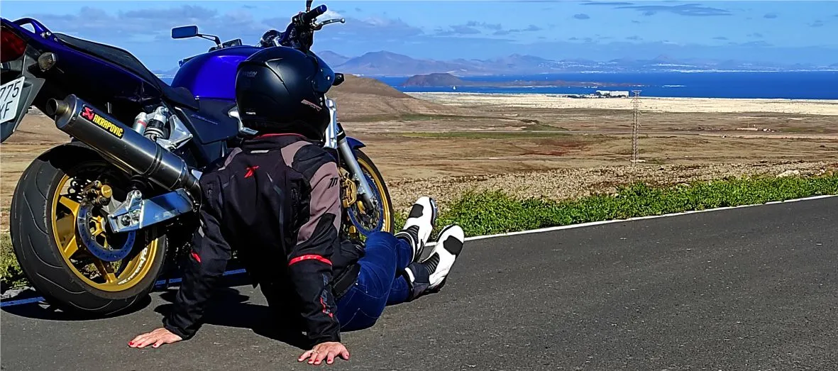 Female rider stopped on a scenic secondary road at a viewpoint overlooking the Corralejo dunes, Lobos Island and Lanzarote during a motorcycle tour in Fuerteventura.