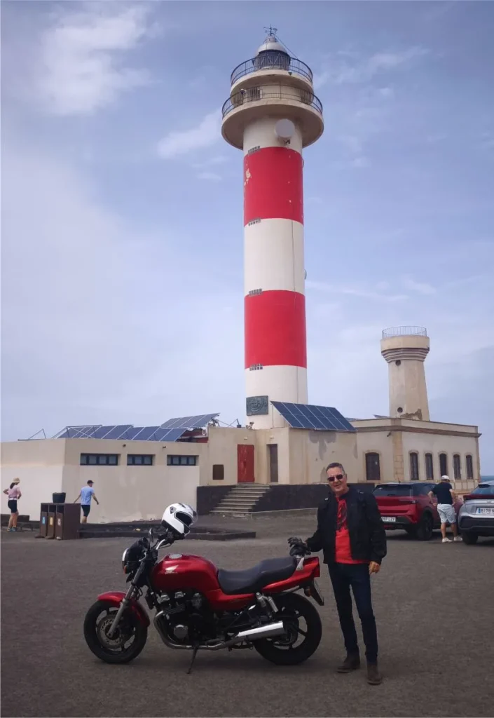 Tourist with a red retro Honda CB750 parked at El Cotillo lighthouse during a motorcycle tour in Fuerteventura.